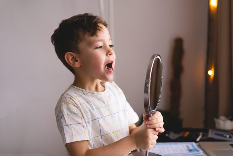 boy practicing articulation therapy in the mirror