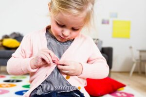 girl buttoning her sweater while practicing her dressing skills